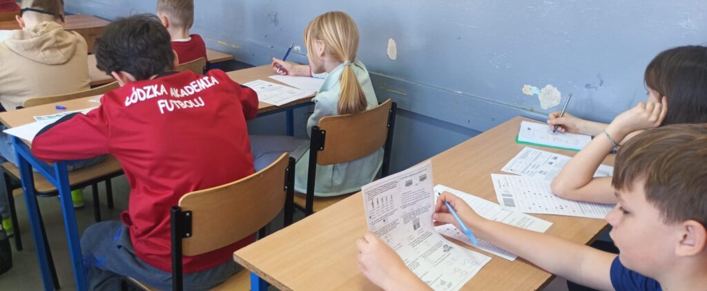 Uczniowie siedzą w klasie w ławkach nad arkuszami konkursowymi.