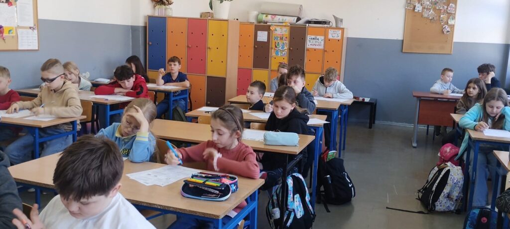 Uczniowie siedzą w klasie w ławkach nad arkuszami konkursowymi.