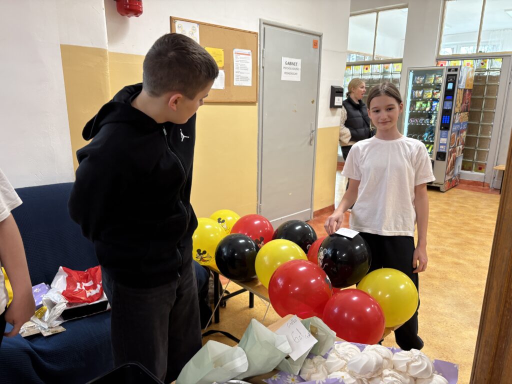 uczennica i uczeń stoją obok kolorowych balonów