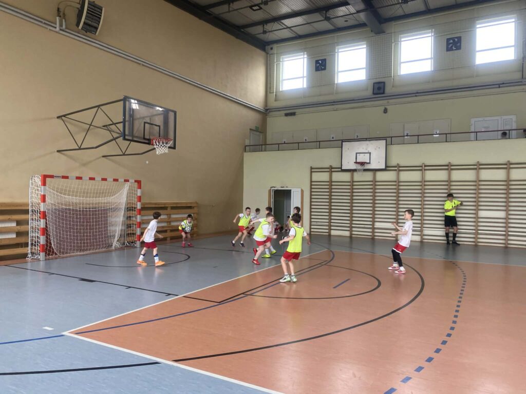 uczniowie grają w piłkę nożną na hali, drużyny w żółtych i białych koszulkach