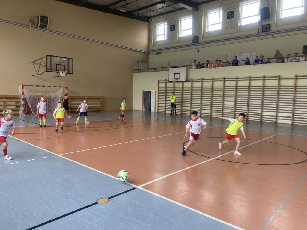 uczniowie grają w piłkę nożną na hali, drużyny w żółtych i białych koszulkach
