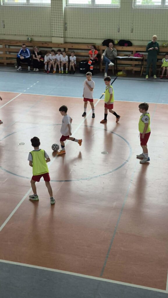 uczniowie grają w piłkę nożną na hali, drużyny w żółtych i białych koszulkach