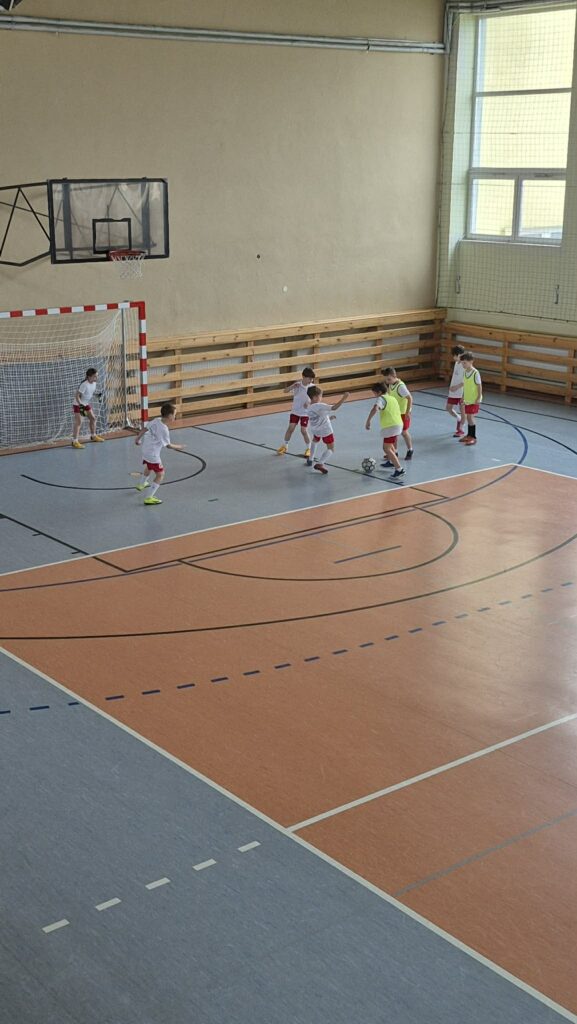 uczniowie grają w piłkę nożną na hali, drużyny w żółtych i białych koszulkach