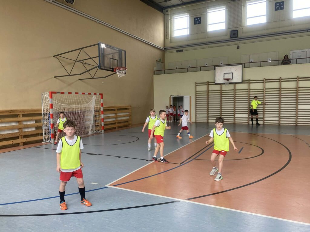 uczniowie grają w piłkę nożną na hali, drużyny w żółtych i białych koszulkach