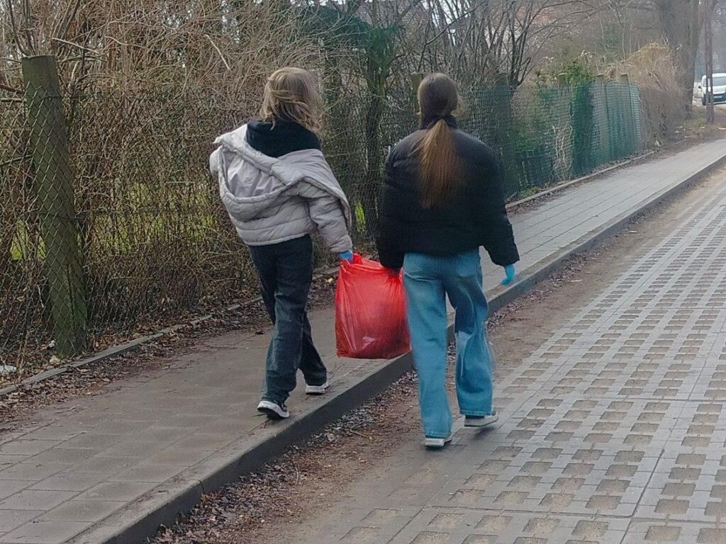 zdjęcie przedstawia dwie uczennice od tyłu niosące worek ze śmieciami