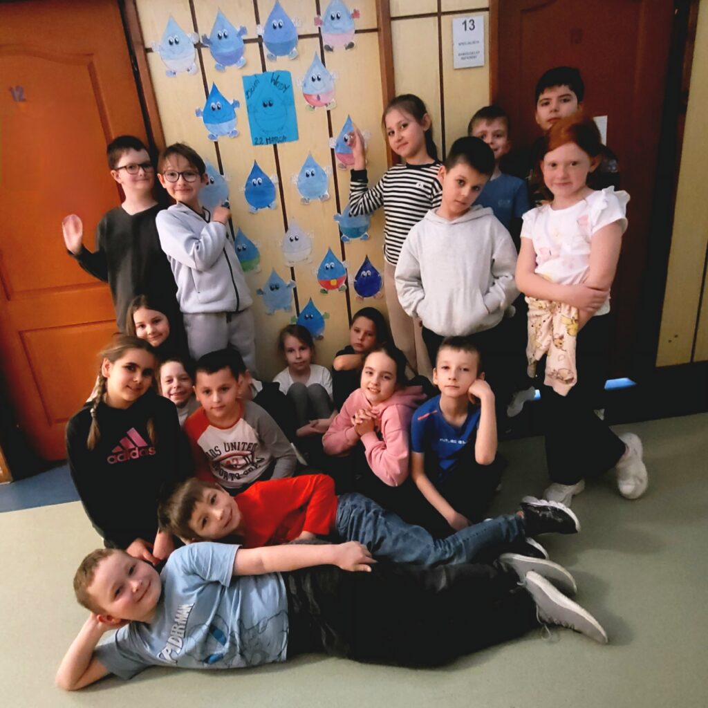 zdjęcie grupowe uczniów, stoją i kucają przy ścianie z naklejonymi kropelkami wody