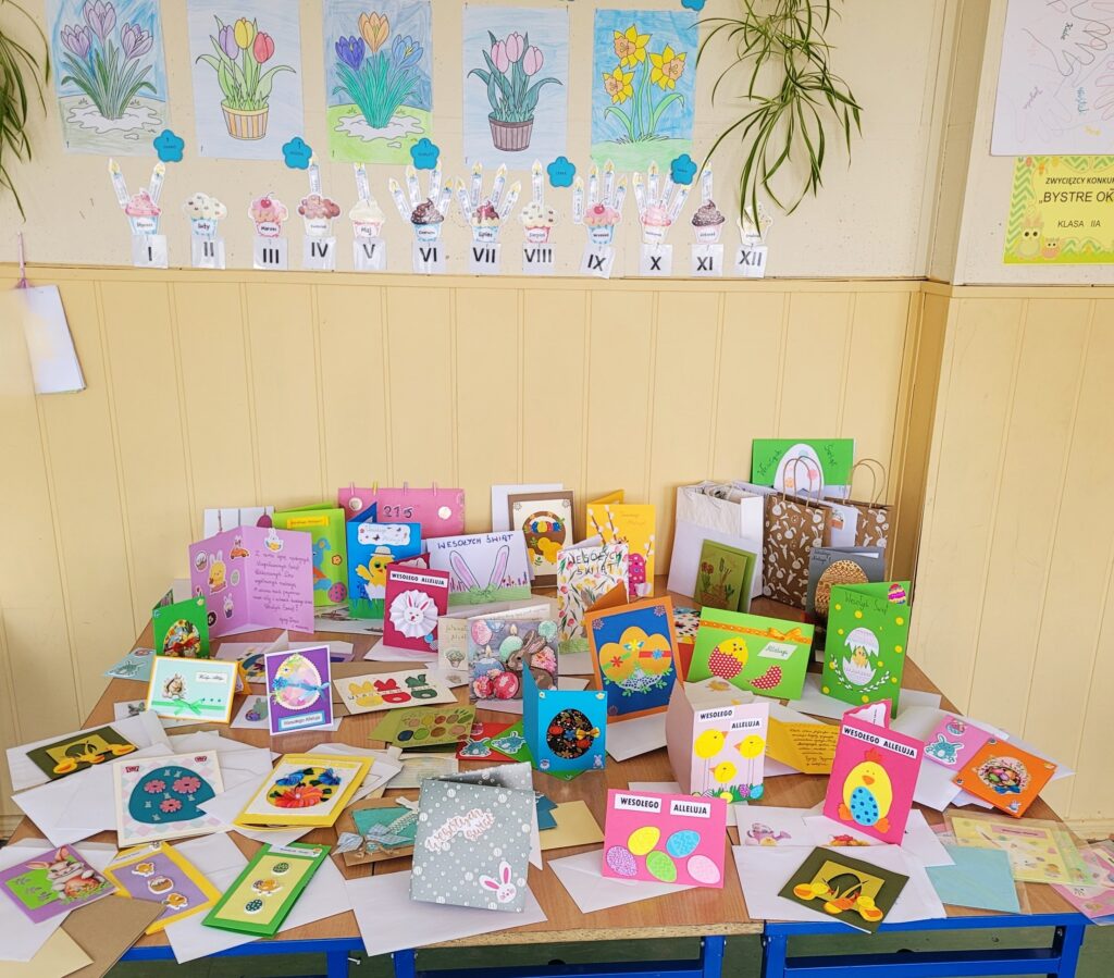 Kolorowe świąteczne kartki "Podaruj świąteczne życzenia" - Wielkanoc, ustawione na ławkach w sali lekcyjnej.