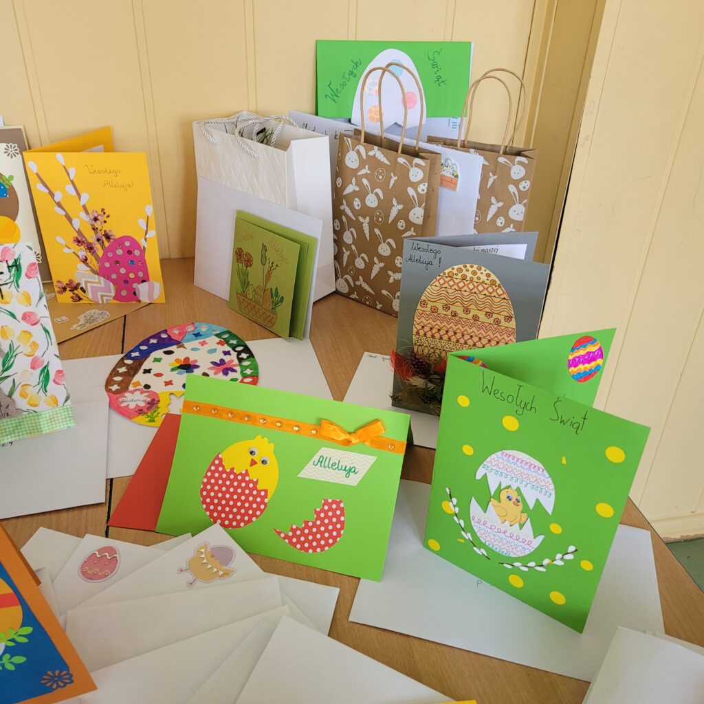 Kolorowe świąteczne kartki "Podaruj świąteczne życzenia" - Wielkanoc, ustawione na ławkach w sali lekcyjnej.