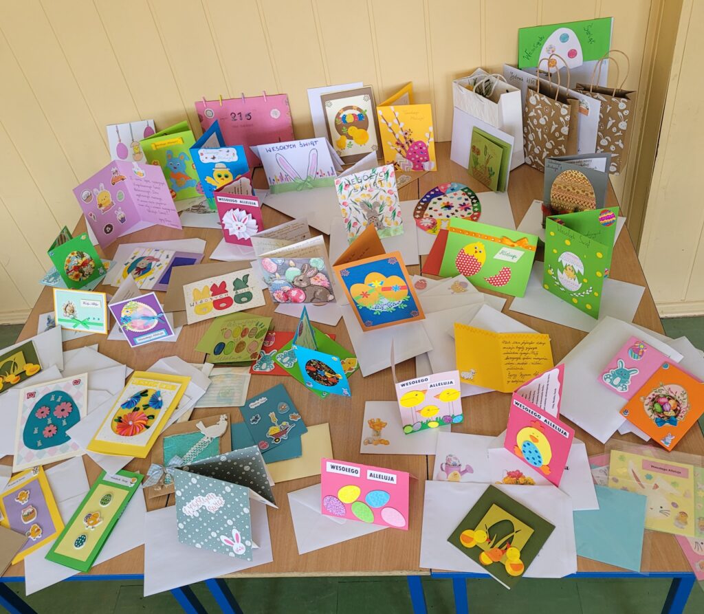 Kolorowe świąteczne kartki "Podaruj świąteczne życzenia" - Wielkanoc, ustawione na ławkach w sali lekcyjnej.