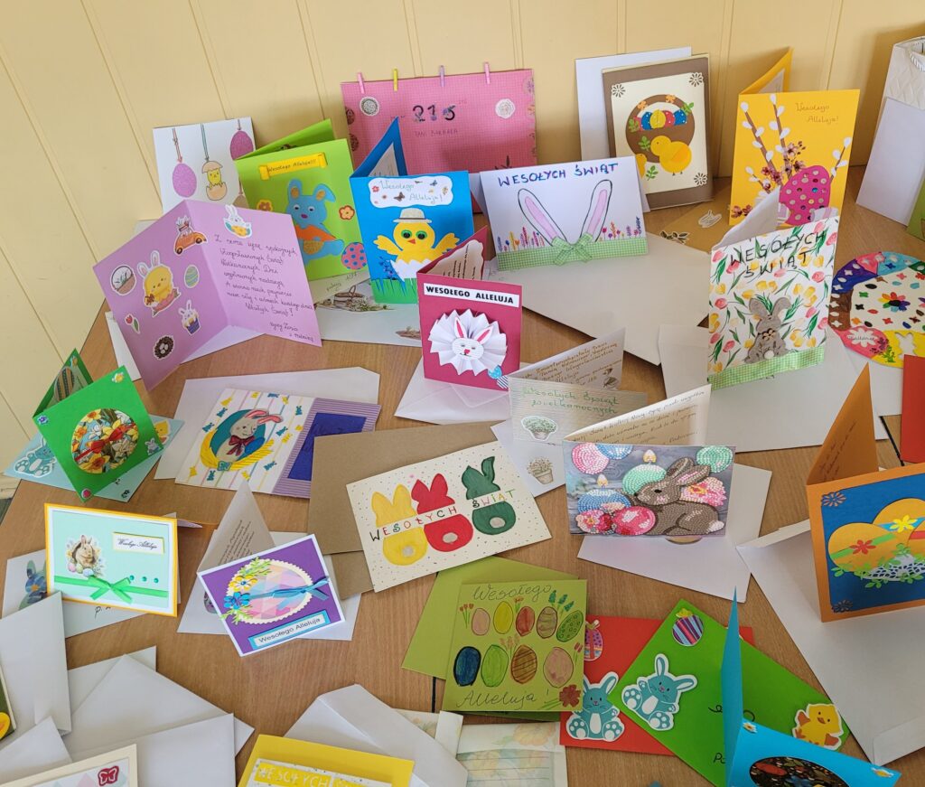 Kolorowe świąteczne kartki "Podaruj świąteczne życzenia" - Wielkanoc, ustawione na ławkach w sali lekcyjnej.