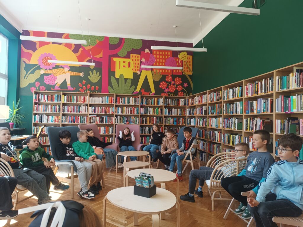 uczniowie siedzą w bibliotece na różnych fotelach i rozmawiają 