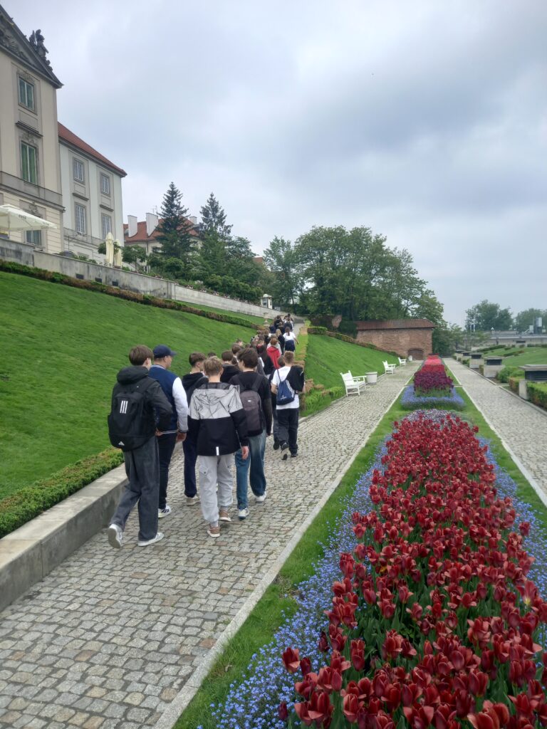 dzieci idą chodnikiem, obok piękna roślinność kwiatowa
