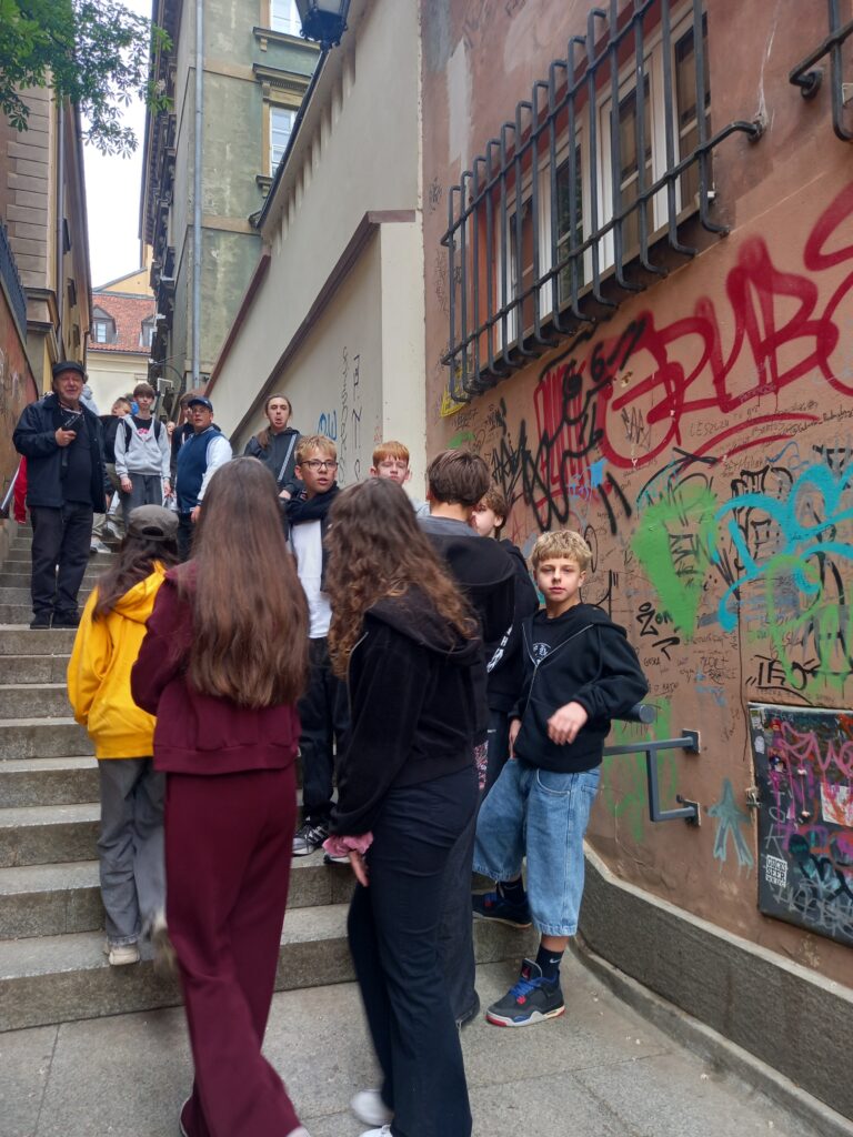 dzieci idą drogą, przechodzą obok ściany wymazanej grafiti