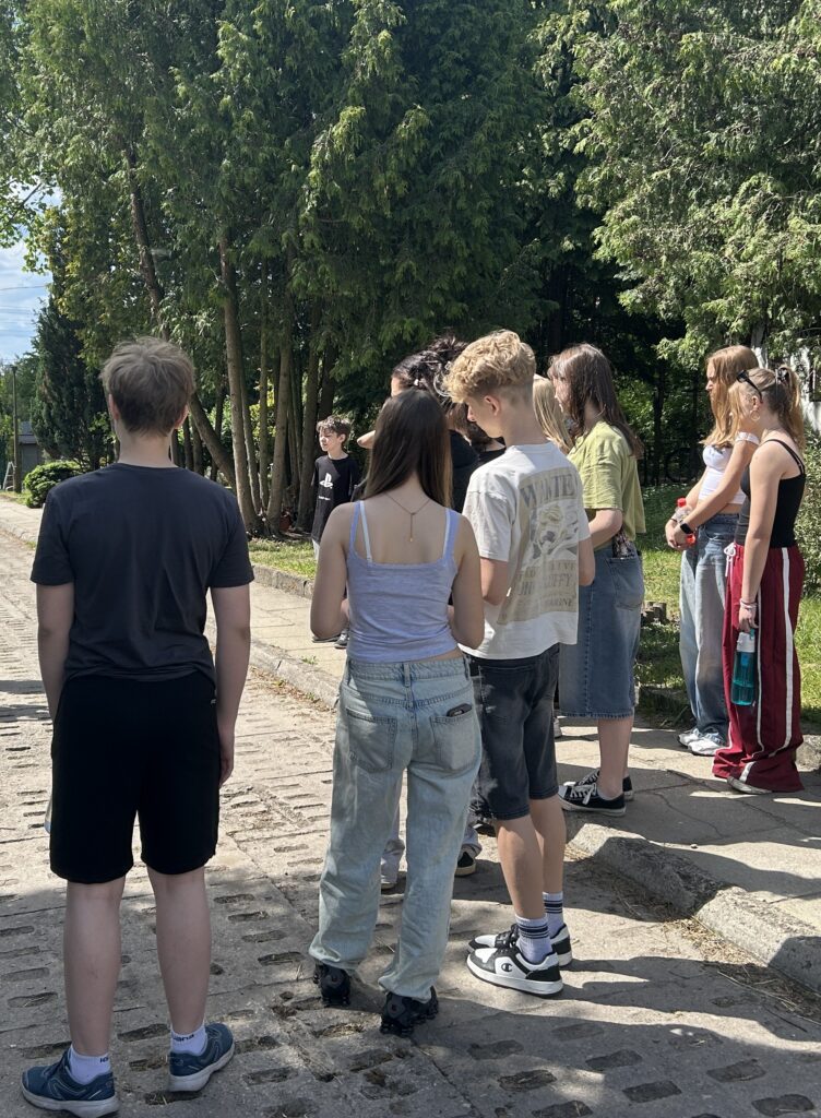 dzieci stoją tyłem do aparatu i słuchają opowiadania starszych uczniów