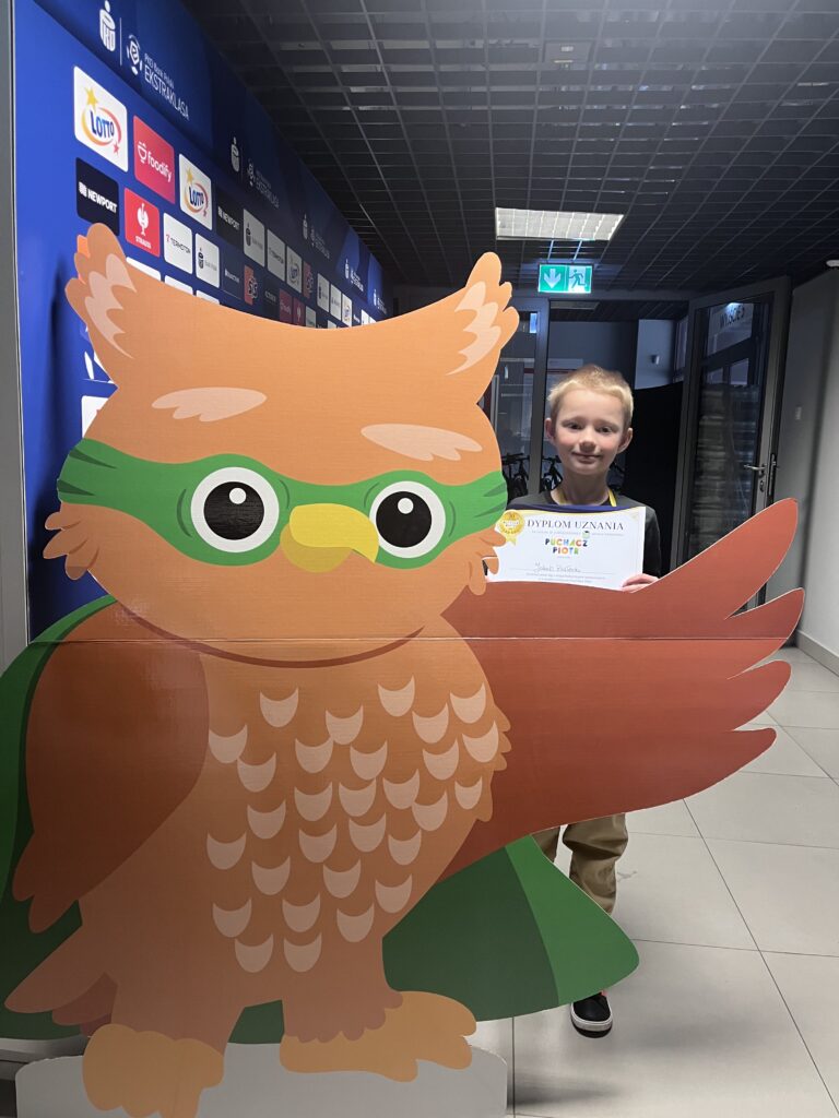uczeń trzyma dyplom i medal, stoi obok dużego rysunku sowy