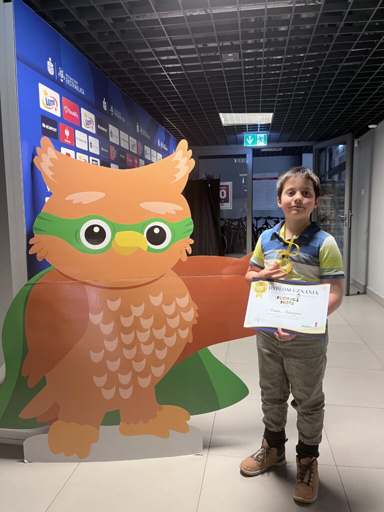 uczeń trzyma dyplom i medal, stoi obok dużego rysunku sowy