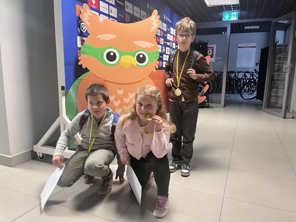 troje uczniów stoi obok rysunku sowy