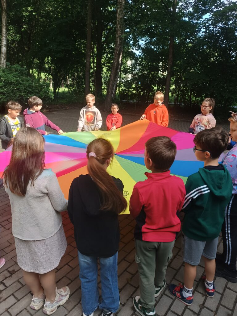 dzieci trzymają materiał kolorowy, stoją w kole