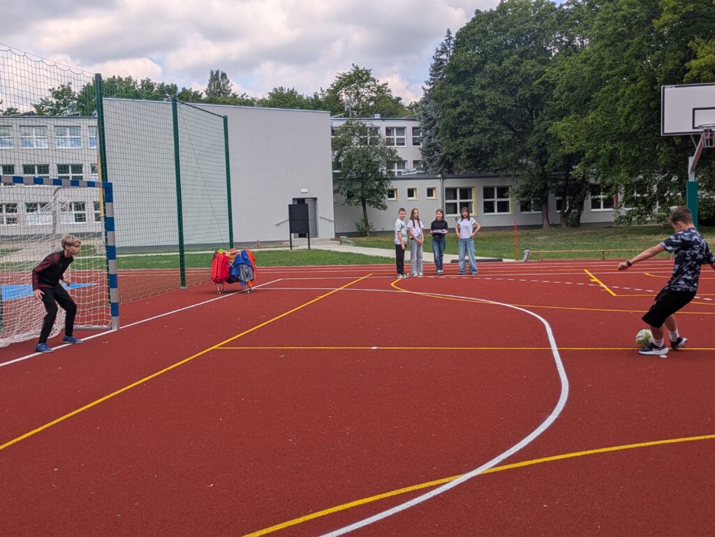 jeden uczeń stoi w bramce i broni, drugi strzela