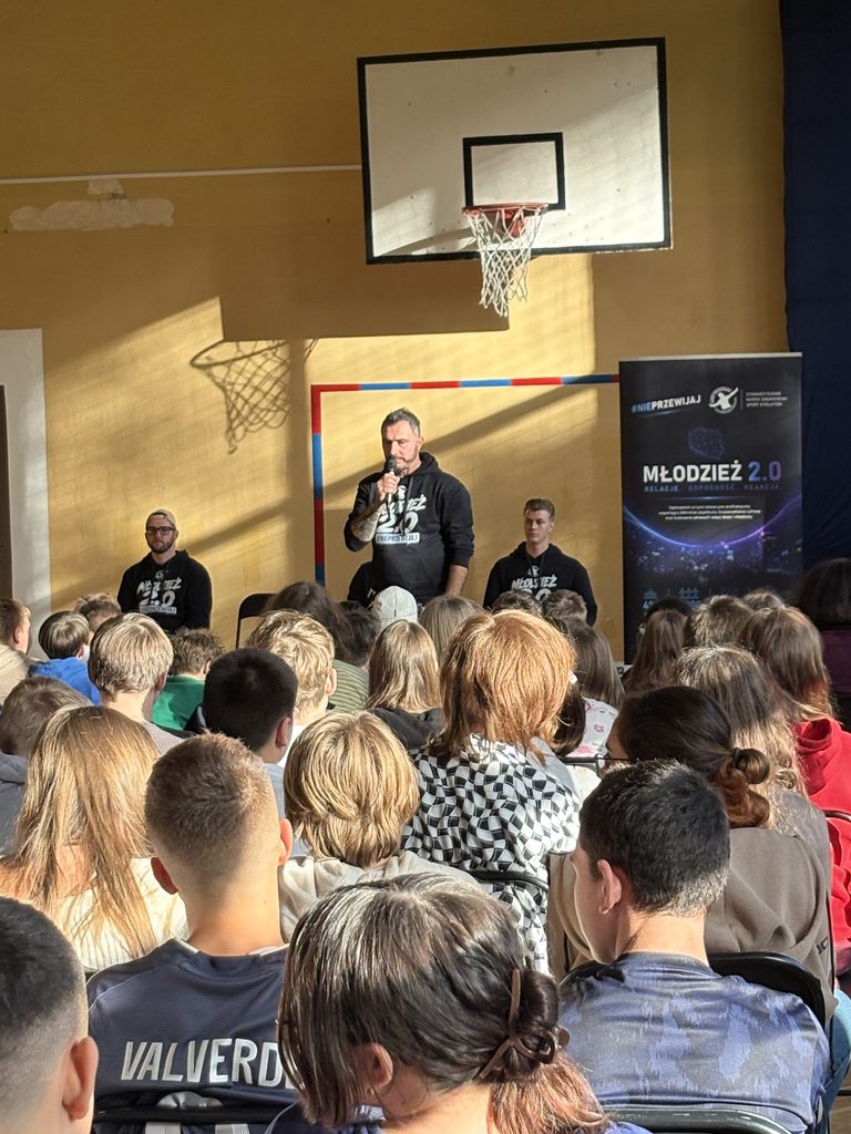 pan Marek przemawia do młodzieży siedzącej w sali gimnastycznej