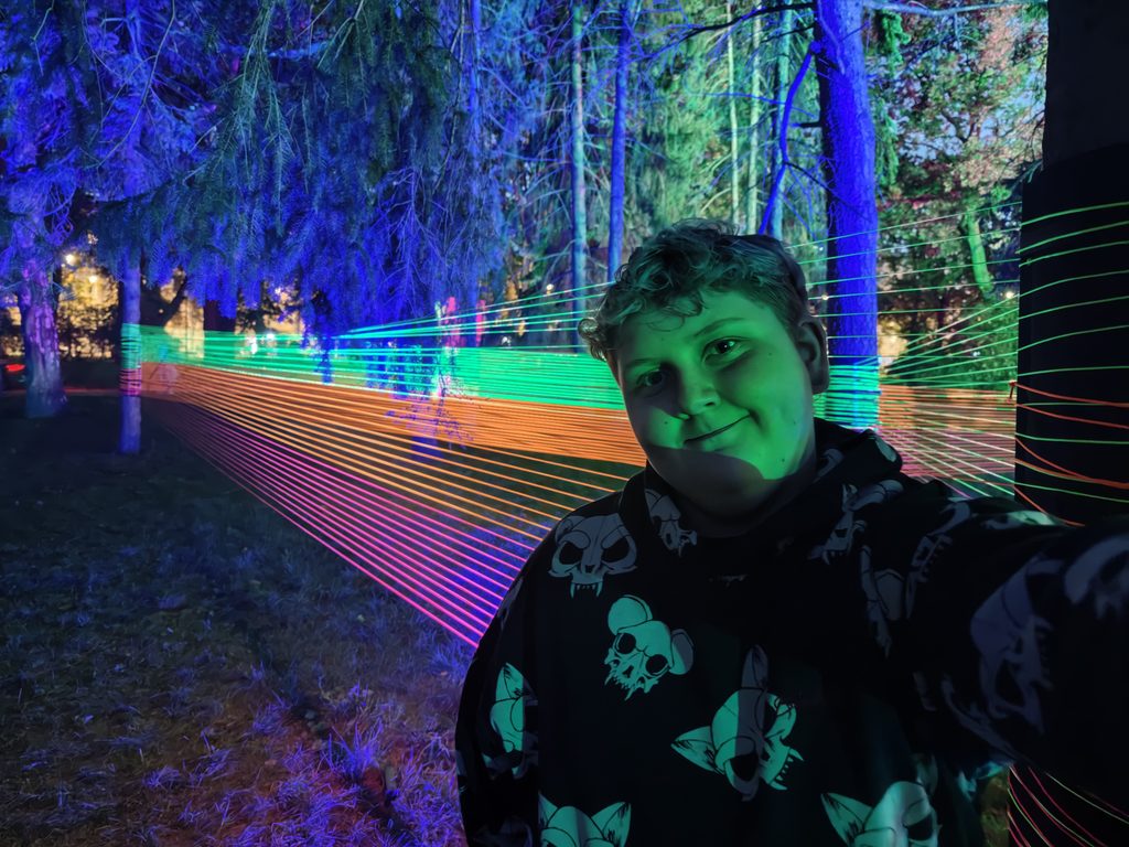 Julek Kiełbasiński - Park Staromiejski  chłopiec na tle kolorowej zielono-pomarańczowo-różowej instalacji wokół drzew